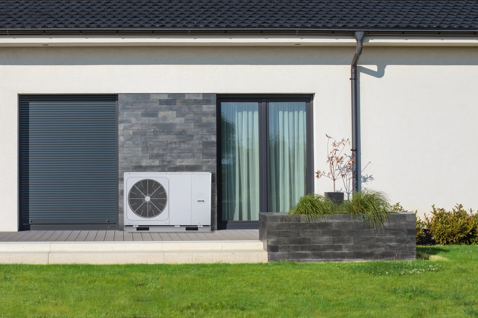 Façade de maison moderne avec unité extérieure de pompe à chaleur air-eau installée sur terrasse carrelée