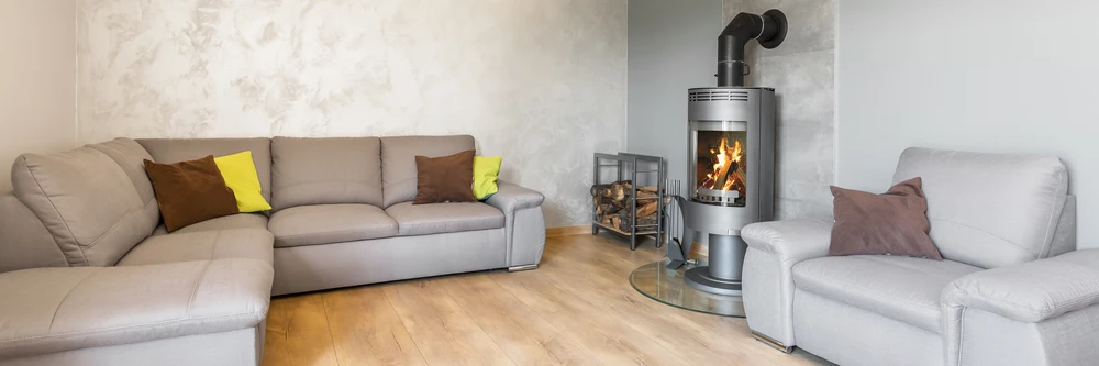 Salon moderne avec poêle à bois en fonctionnement, canapé gris et fauteuil assorti, coussins décoratifs jaunes et marrons