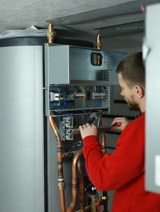 Technicien en combinaison rouge effectuant la maintenance d'une chaudière domestique dans un local technique