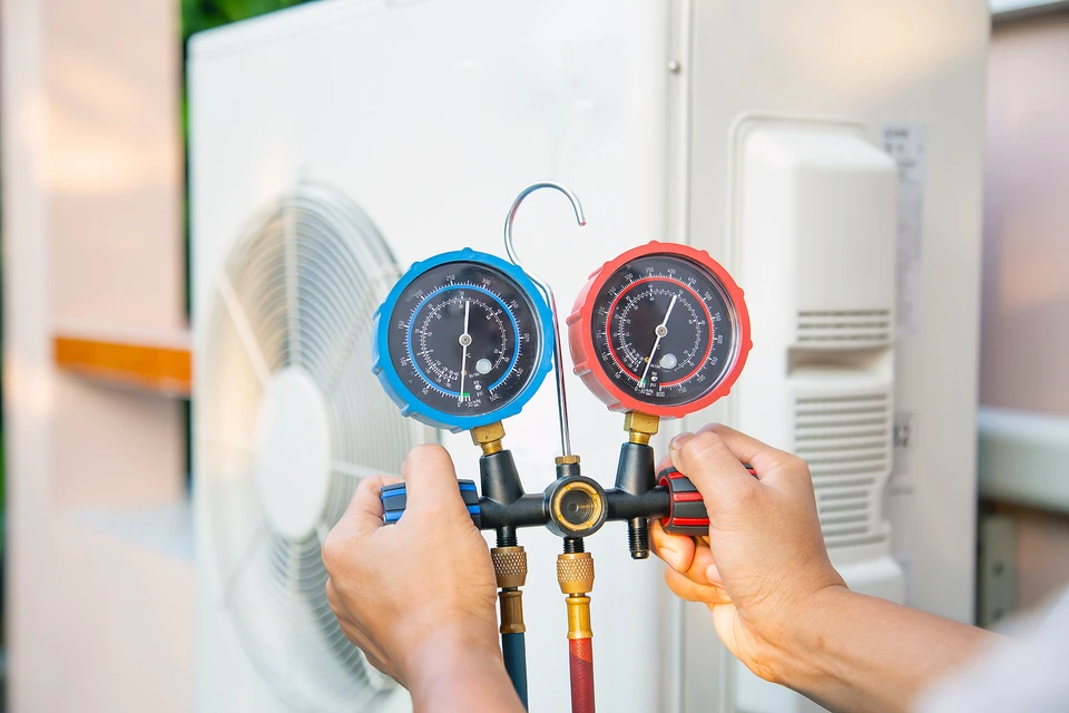 Technicien tenant un manifold de climatisation avec deux manomètres à cadrans colorés bleu et rouge dans un environnement intérieur professionnel