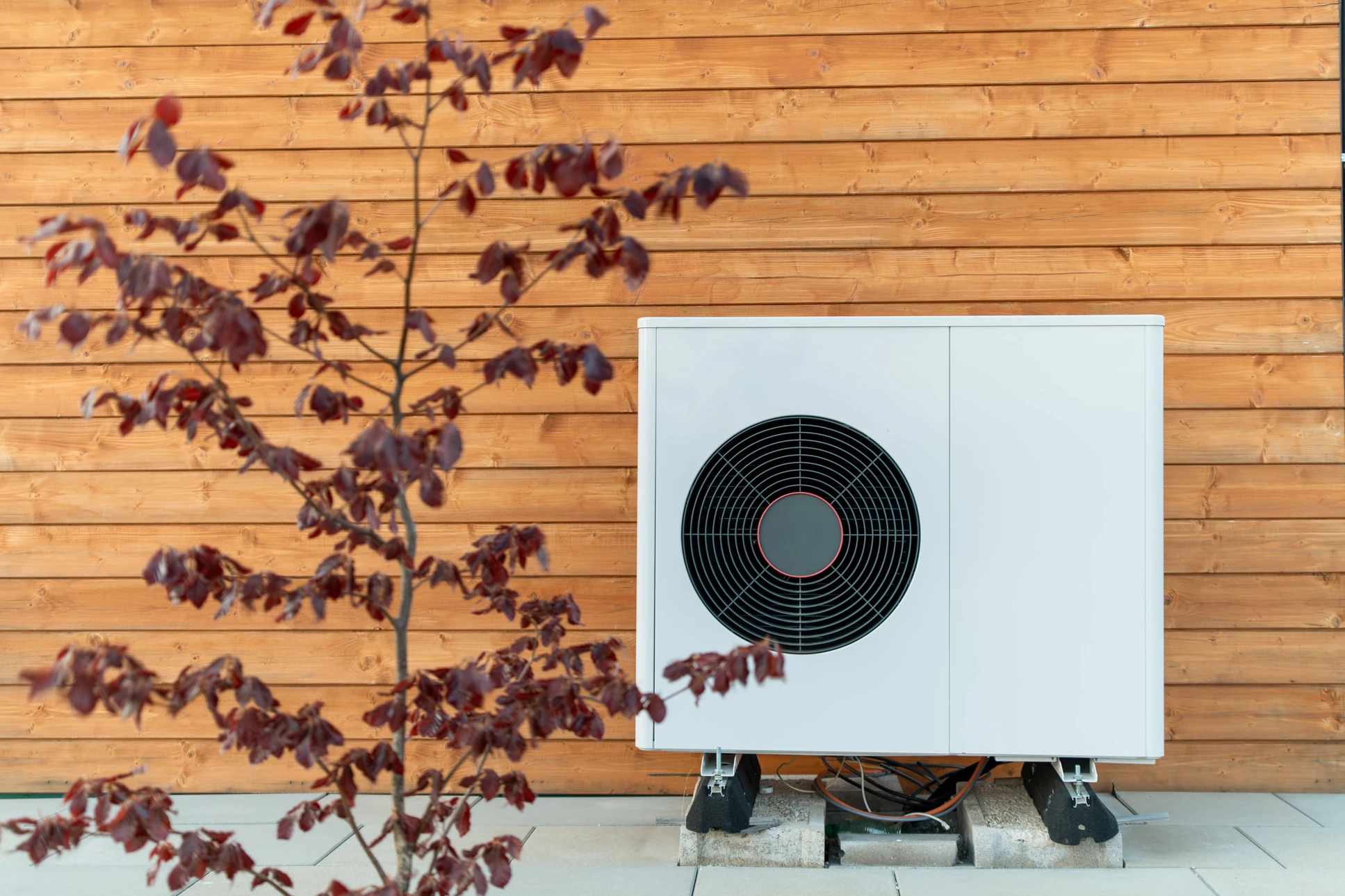 Ext&eacute;rieur r&eacute;sidentiel moderne avec pompe &agrave; chaleur air-eau install&eacute;e sur socle b&eacute;ton contre fa&ccedil;ade blanche