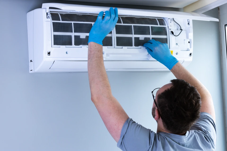 Technicien souriant effectuant la maintenance d'une climatisation murale split dans un intérieur résidentiel moderne